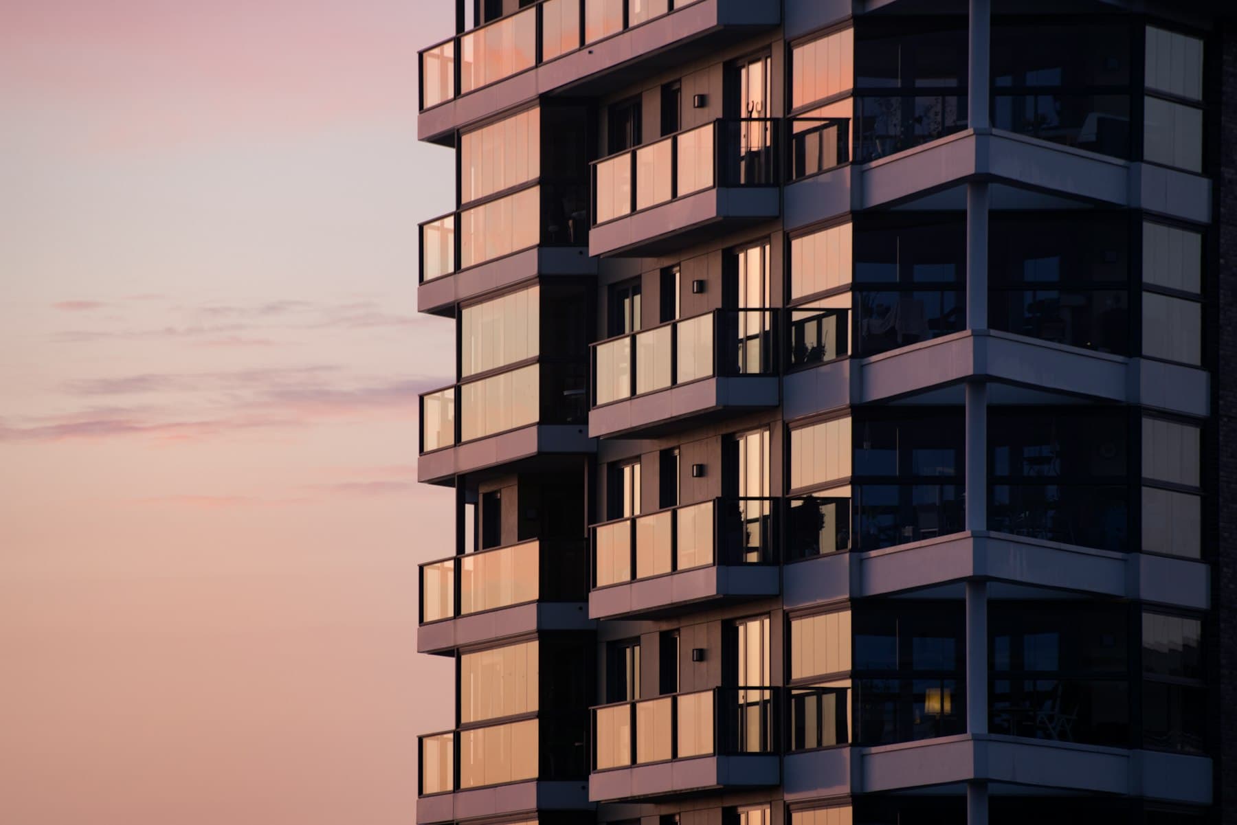 Modern apartment building with glass balconies at sunset